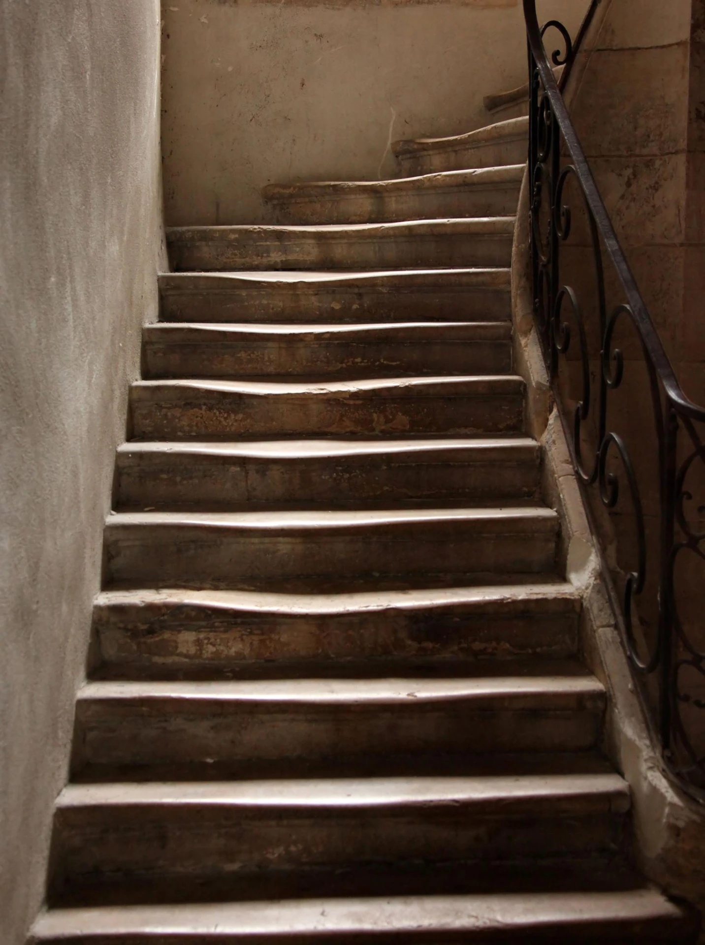 A worn stone staircase with a wrought-iron railing, dimly lit, steps hollowed by centuries of use