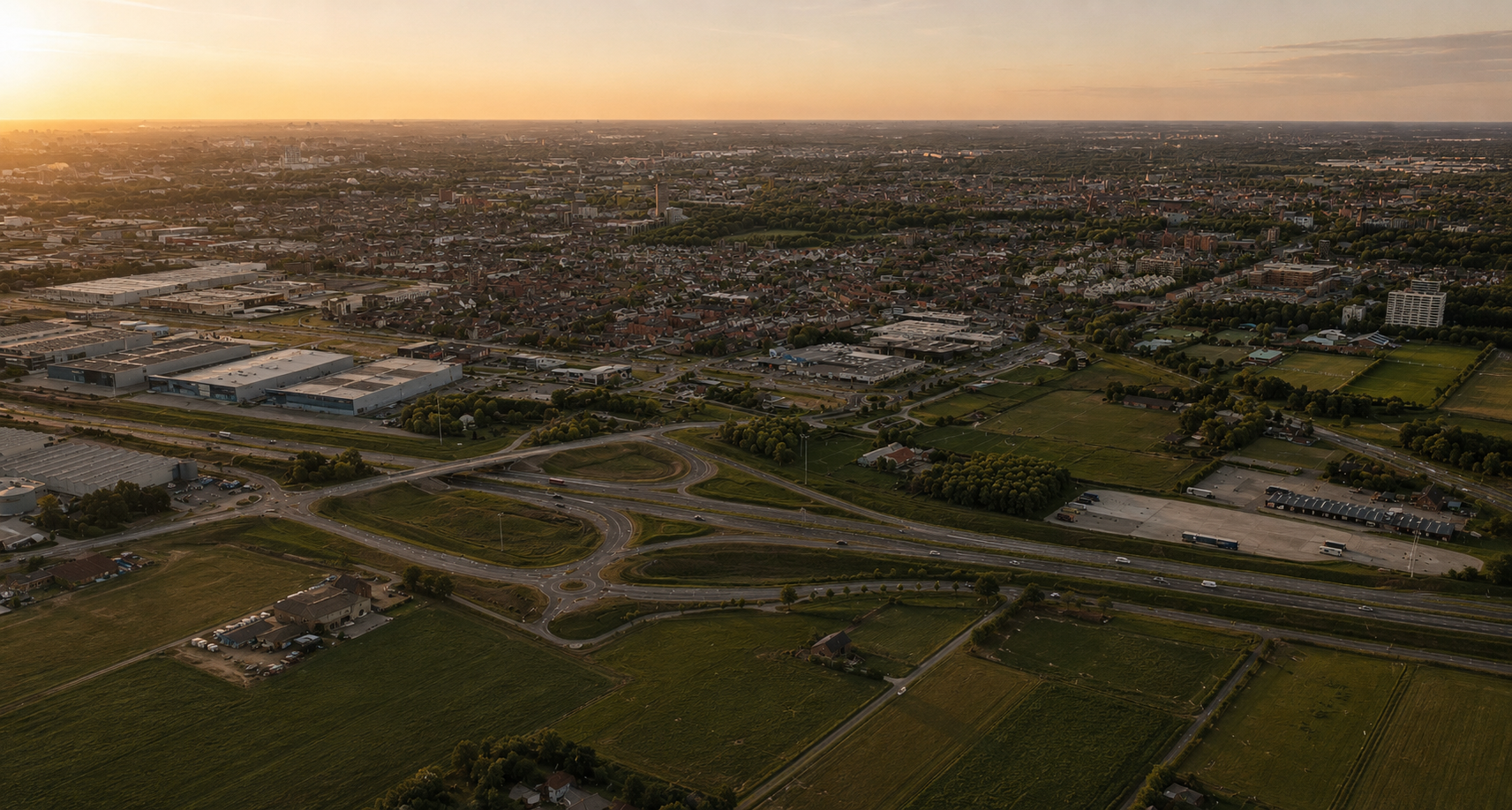 Aerial view at dusk of a highlighted land position bordering a Dutch city edge, fields and infrastructure around it